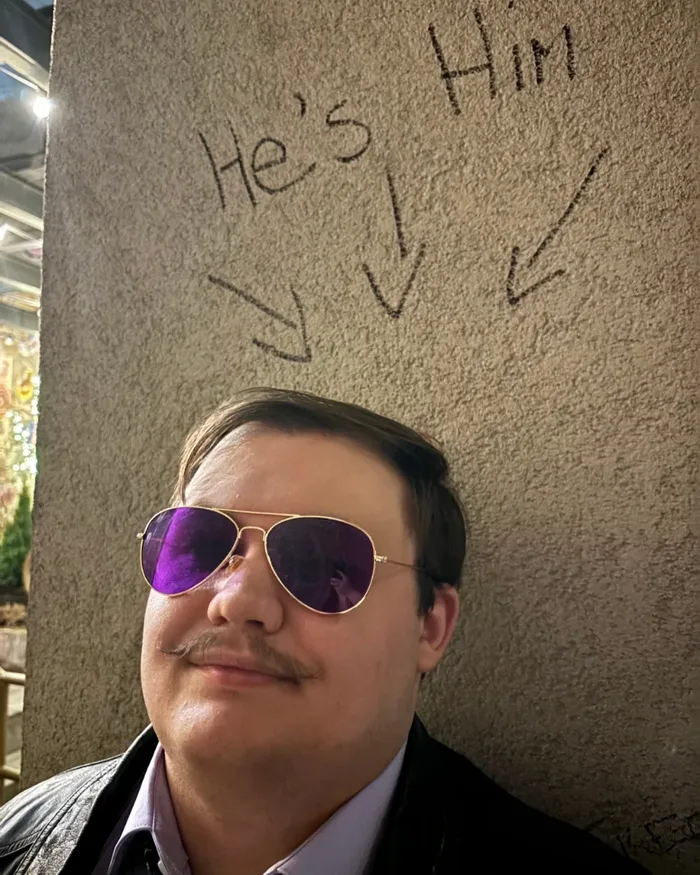Noah wearing purple sunglasses under wall graffiti pointing toward him